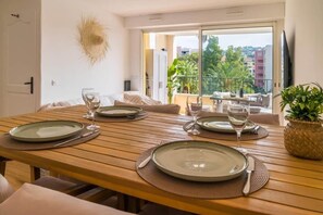A dining area with a wooden table set for four, a balcony with a view of buildings and greenery, and a television on the wall. - Renovated apartment with a pool, 250 meters from the beach (Sainte-Maxime)