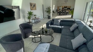 En moderne stue med en hjørnesofa, lænestole og et sofabord. I baggrunden er der et spiseområde med et køkken.