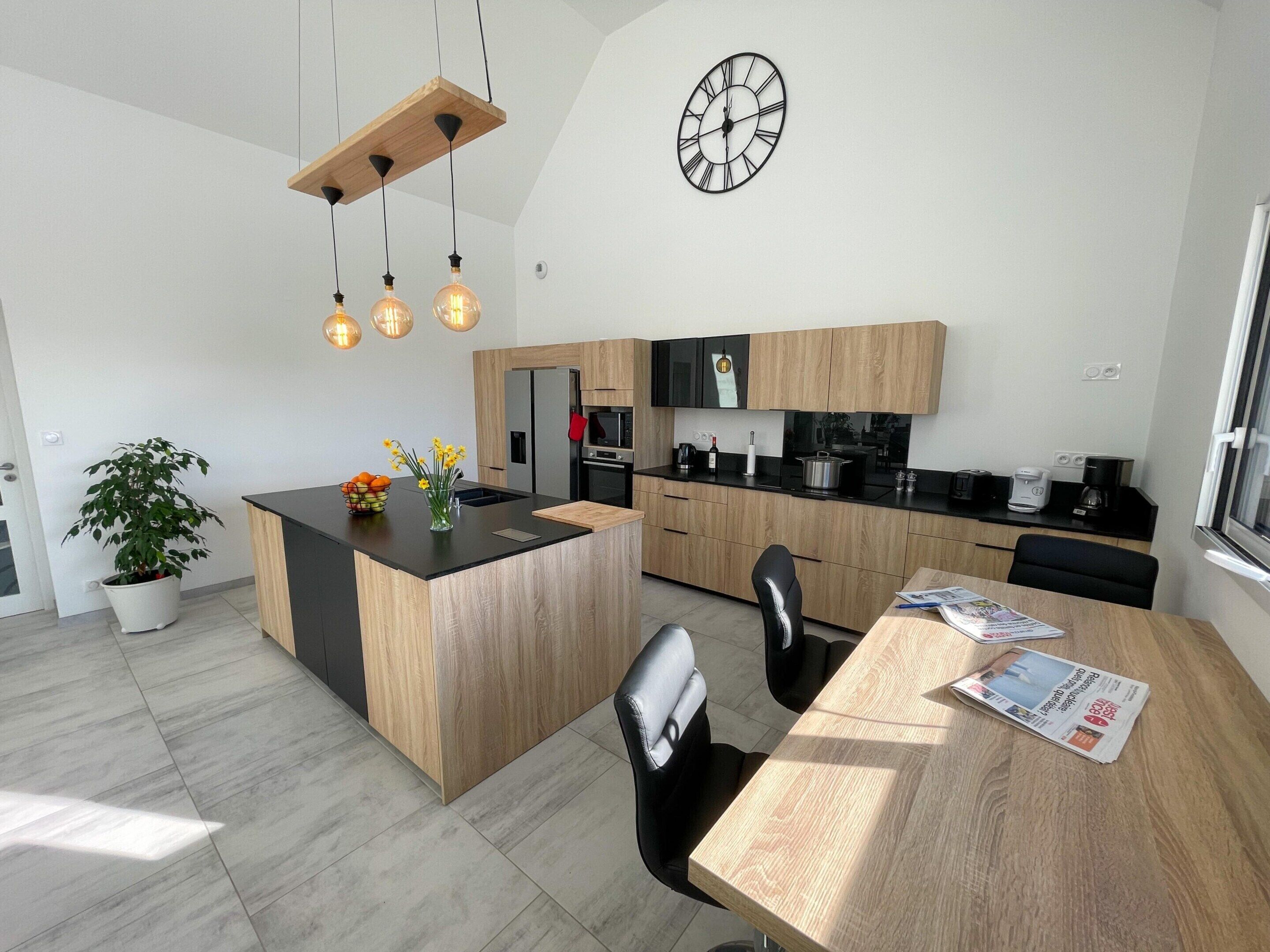 A modern kitchen with a central island, wooden cabinets, a built-in oven, and a hanging light fixture.