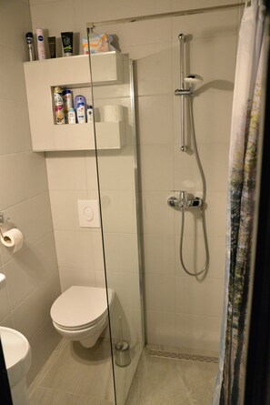 Une salle de bain comprenant des toilettes, une douche en verre et une étagère avec des articles de toilette.