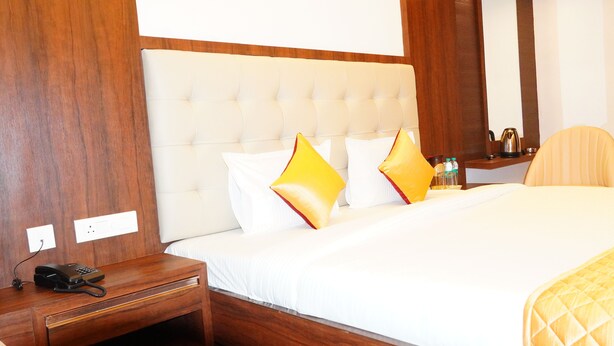 Una habitación de hotel con una cama grande, una mesita de noche de madera con un teléfono y una silla.