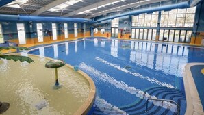 An indoor swimming pool with clear water, a diving board, and a water fountain.