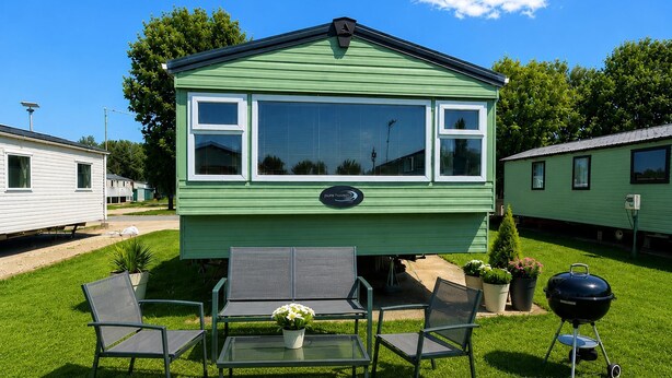 A green mobile home with a patio area, including a table and chairs, and a barbecue grill.