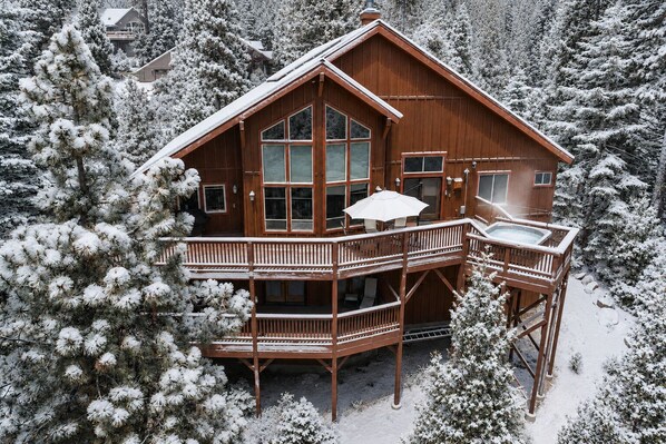 Une cabane en bois dotée d’un balcon et d’un jacuzzi, entourée d’arbres couverts de neige.