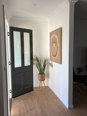 En hall med en mörk dörr, en krukväxt och ett inramat konstverk på väggen.