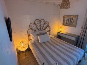 A bedroom with a bed, bedside lamps, a nightstand, a wall-mounted picture, and a hanging light fixture. - VILLA PETREL (Saint-Paul)