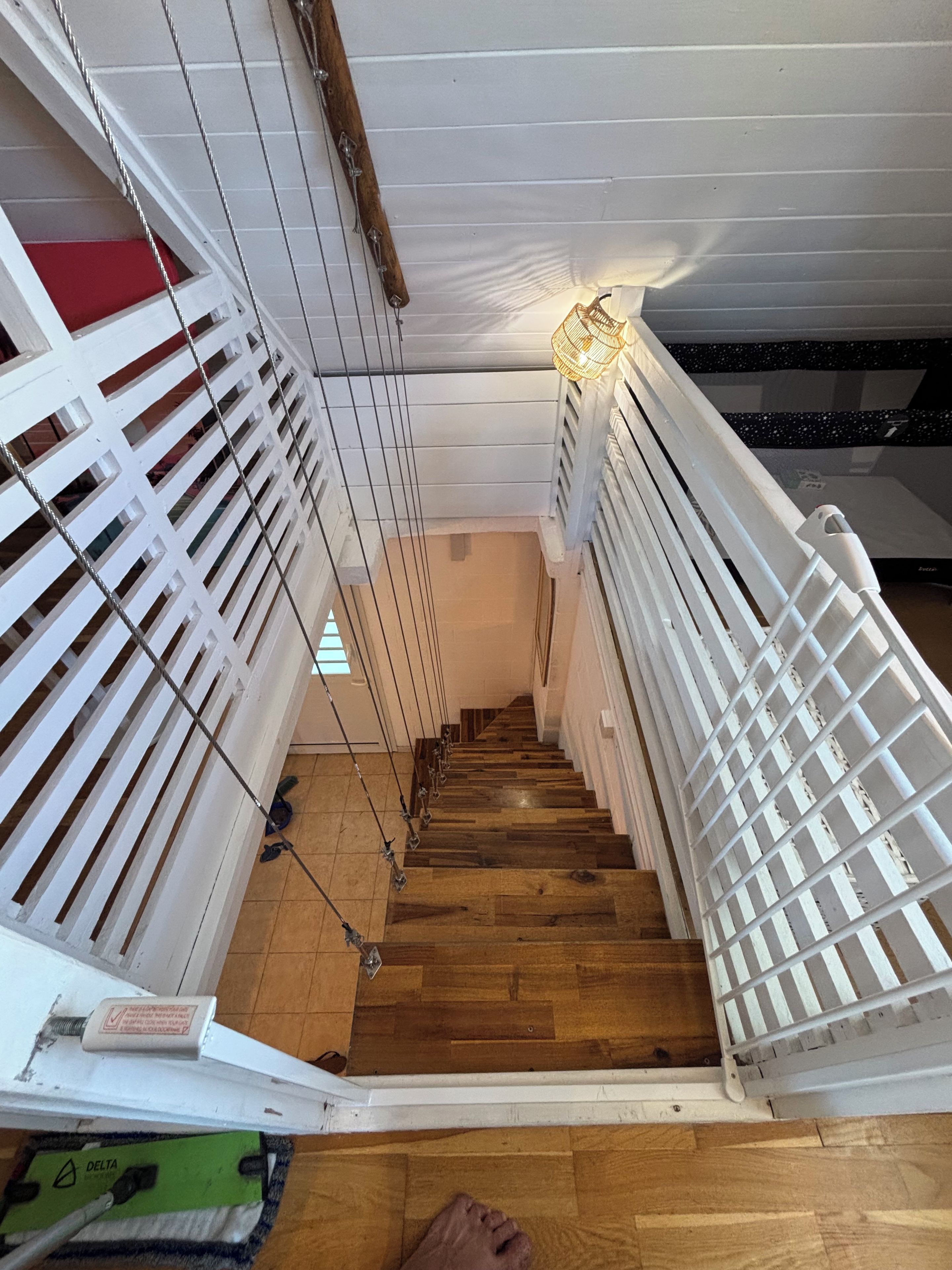 Una scala in legno con ringhiere bianche, un lampadario in cima e un oggetto rosso a sinistra.