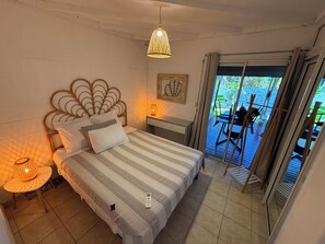 Une chambre à coucher avec un lit, une lampe de chevet et une vue sur une terrasse extérieure aménagée avec des chaises et une table.