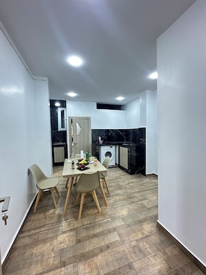 A modern kitchen with a washing machine, a dining area with a table and chairs, and a door leading to another room. - Skikda Rentals (Skikda)