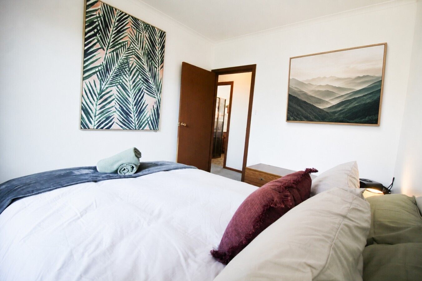 A bedroom with a bed, a door, and two wall-mounted paintings.