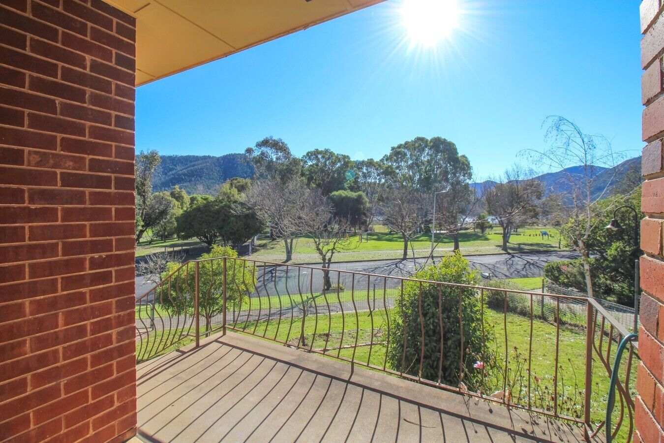 A balcony with a view of a park, a river, and distant hills.