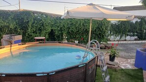 An outdoor swimming pool with a ladder, surrounded by greenery and a patio area. - "El Filali" House (Villaminaya)
