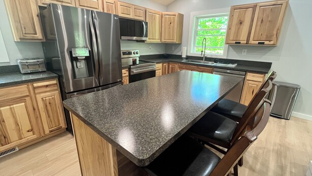 Una cocina moderna con encimeras de granito, electrodomésticos de acero inoxidable, armarios de madera y una isla grande con taburetes de bar.