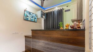 Ein Empfangsbereich mit einem Holzbüro, einem Flachbildfernseher, einem Deckenventilator und einem Schild für den Rezeptionisten.