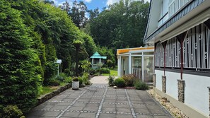 A pathway leading to a building with a conservatory, surrounded by lush greenery and a stone wall.