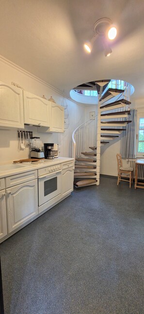 A kitchen with white cabinetry, a built-in oven, a coffee maker, and a spiral staircase leading to a dining area.