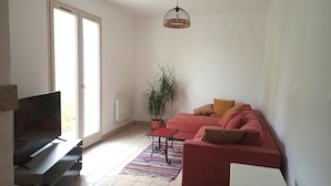 Un salon avec un canapé, un téléviseur, une plante en pot et un luminaire suspendu.