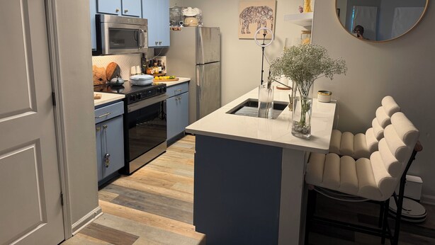 Una cocina con armarios azules, un microondas, un refrigerador y una pequeña isla con un florero.