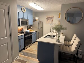 Eine Küche mit blauen Schränken, einer Mikrowelle, einem Kühlschrank und einer kleinen Kochinsel mit einer Vase.