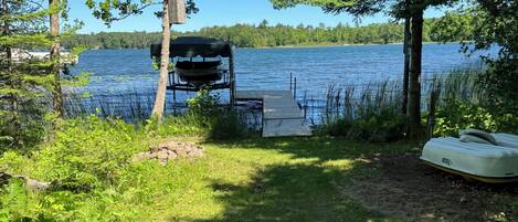 A lakeside dock with a covered seating area, surrounded by trees and vegetation.