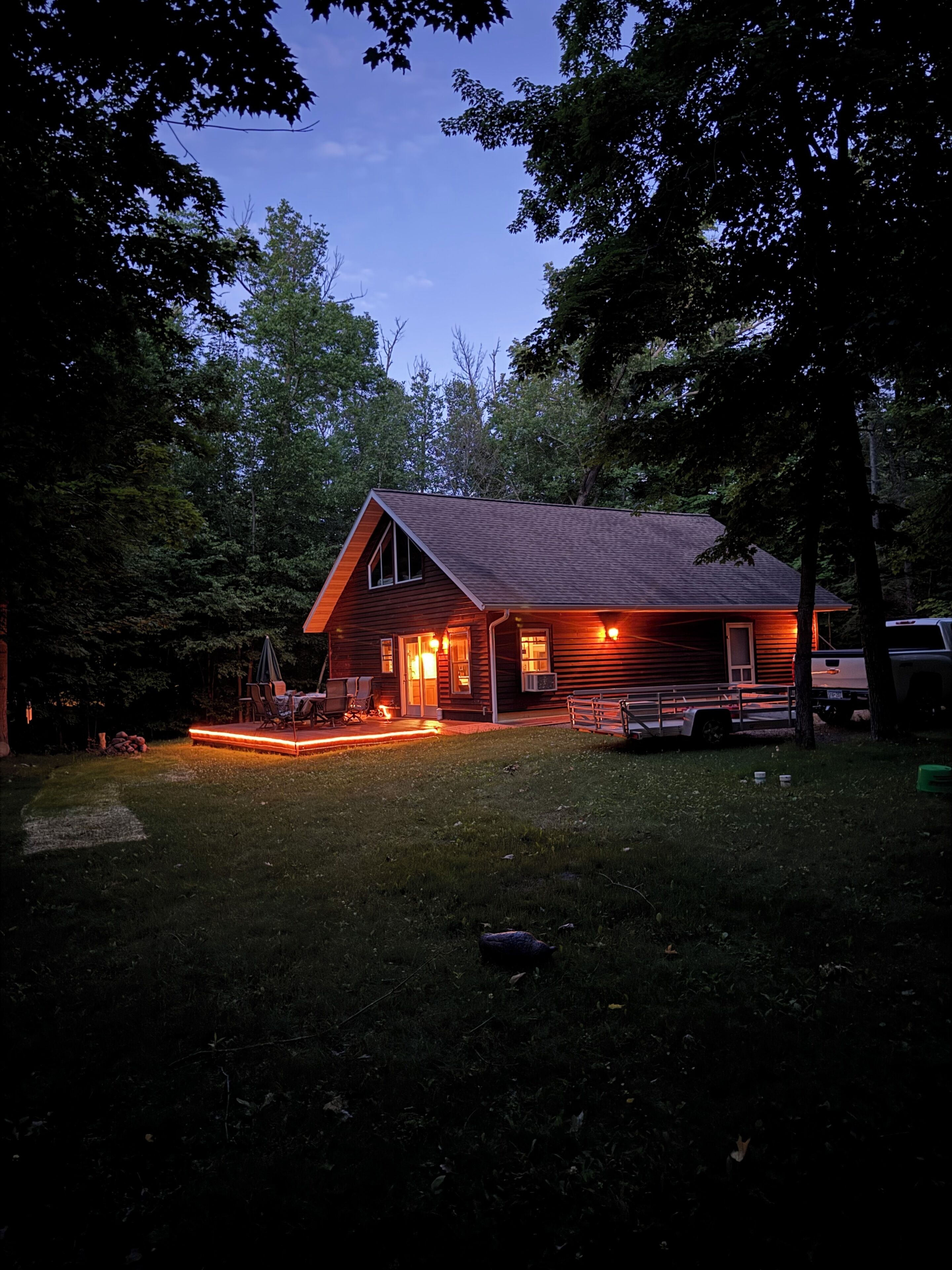 A wooden cabin with a porch, a covered outdoor seating area, and a vehicle parked nearby.