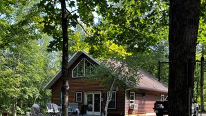 En tvåvånings stuga byggd av trä, med en veranda, omgiven av en välskött gräsmatta och träd.