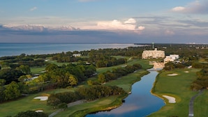 En vy över en golfbana tagen från luften, med en stor byggnad, troligen ett hotell, i bakgrunden.