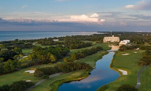 An aerial view of a golf course with a large building, likely a hotel, in the background. - Kiva Dunes Village A unit 103 (Gulf Shores)