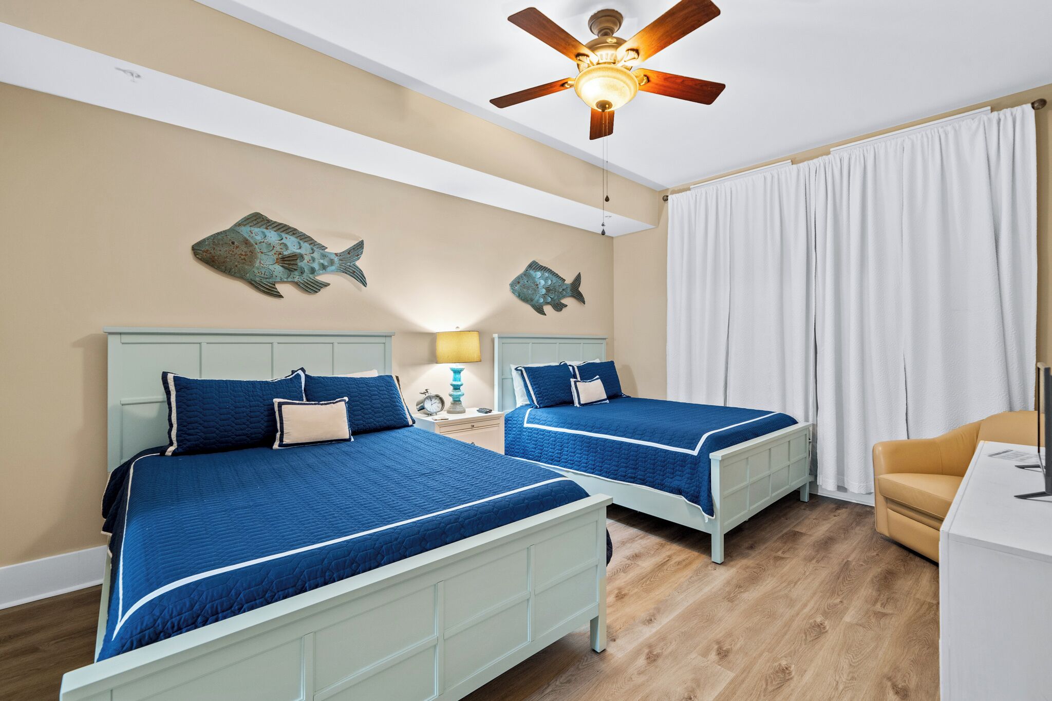A room with two beds, a ceiling fan, and a large window with curtains.