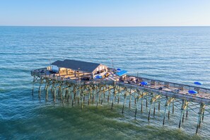 Eine Pier, die ins Wasser führt, mit einem Gebäude am Ende, das Sitzplätze und Sonnenschirme im Freien bietet.
