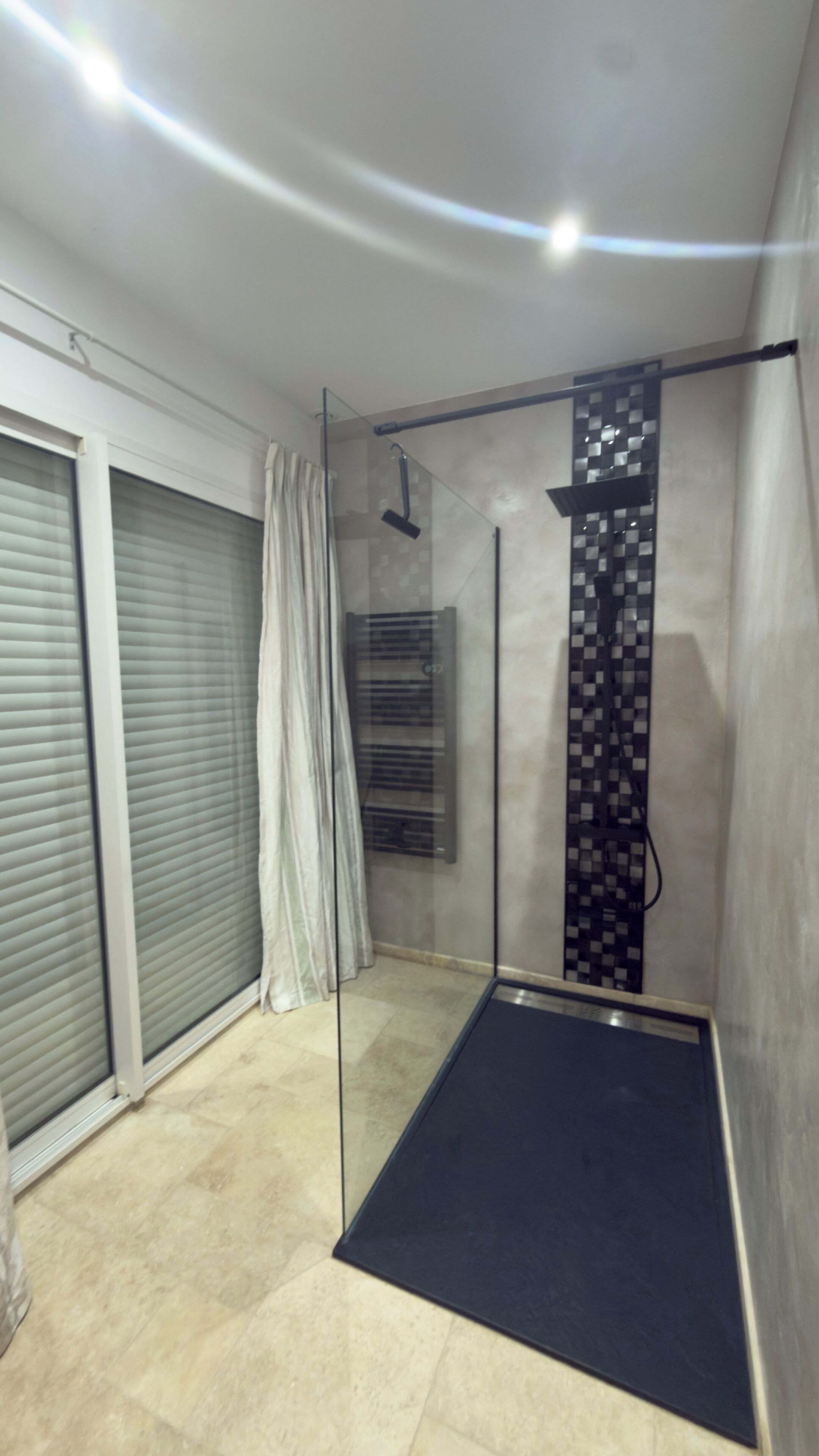 A modern bathroom with a glass shower enclosure, a towel rack, and a tiled floor.