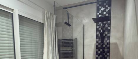 A modern bathroom with a glass shower enclosure, a towel rack, and a tiled floor.