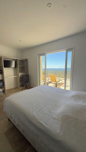 Ein Schlafzimmer mit einem großen Bett, einem Kleiderschrank, einem Fernseher und einer Glastür, die auf eine Terrass mit einem Stuhl führt.