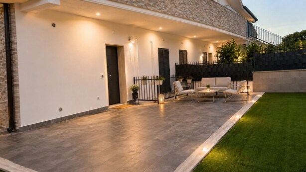 Ein modernes Haus mit überdachter Terrasse, Gartenmöbeln und einem gepflegten Rasen.