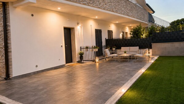 Ein modernes Haus mit überdachter Terrasse, Gartenmöbeln und einem gepflegten Rasen.