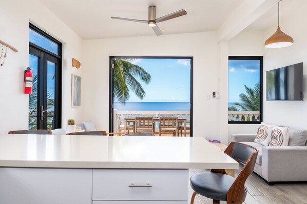 A modern kitchen with a large island, a dining area with wooden furniture, and a view of the ocean.