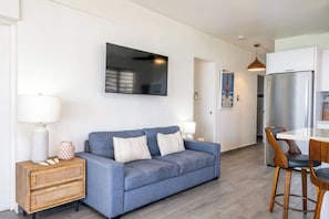 Una sala de estar moderna con un sofá azul, un aparador de madera y una zona de comedor con una mesa blanca y sillas de madera.