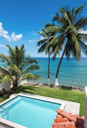 A swimming pool with clear blue water, surrounded by a well-maintained lawn and a view of the ocean.