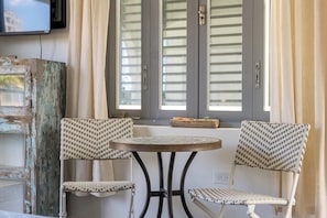 Una habitación con dos sillones de mimbre, una mesita redonda y una ventana con contraventanas.