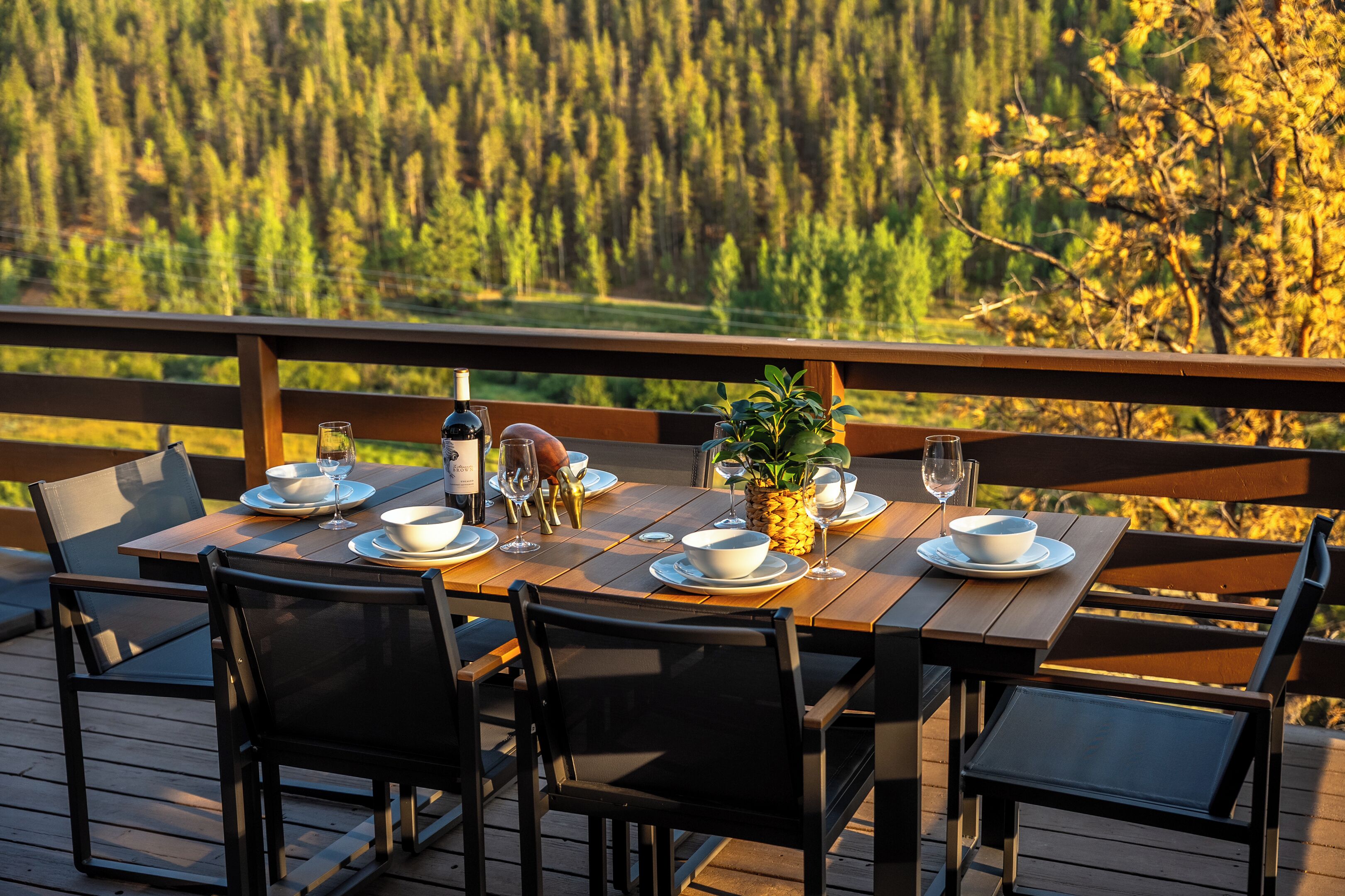Eine Holzterrasse mit einem Esstisch, mit Blick auf eine bewaldete Landschaft.