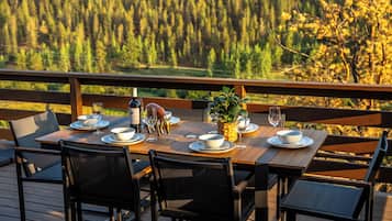 Eine Holzterrasse mit einem Esstisch, mit Blick auf eine bewaldete Landschaft.