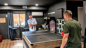 A ping pong table in a room with a window, a wall-mounted air conditioner, and a sign that reads 'High Altitude High Scores.' - Timberline Perch- Hot Tub, Game Room, Bunk Room & Views (Bailey)