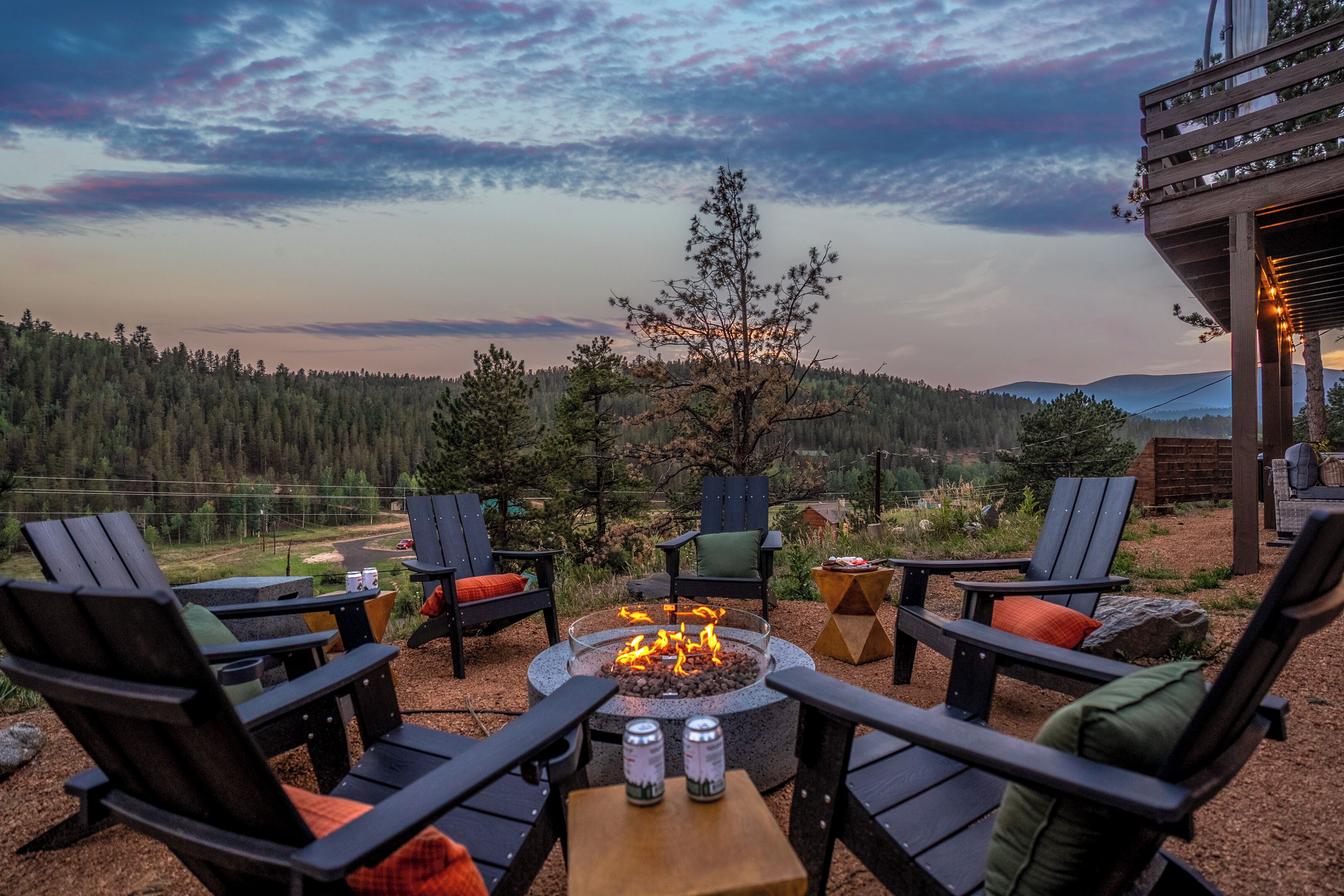 An outdoor seating area with chairs and a fire pit, overlooking a forested landscape.