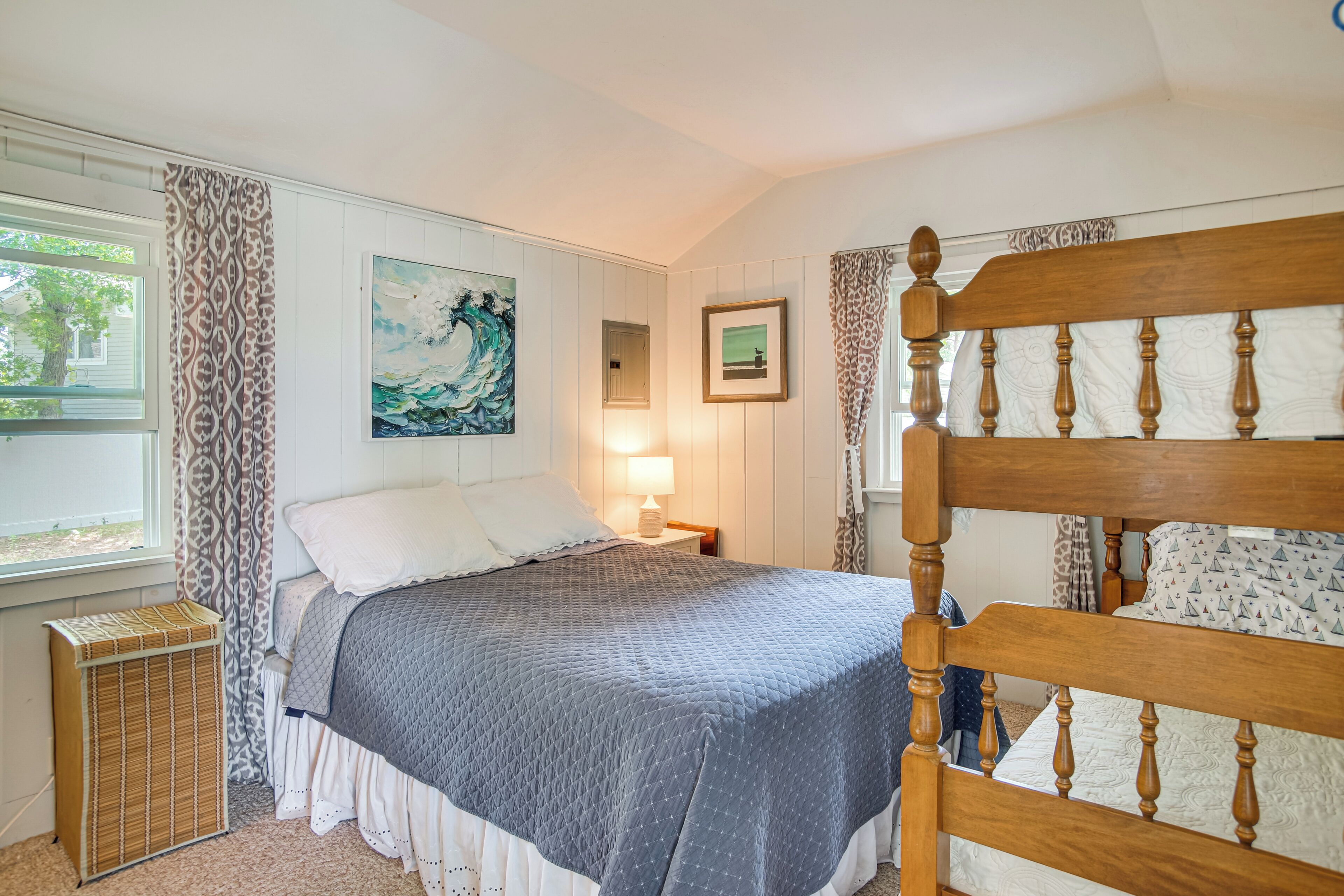 A bedroom with a wooden bed frame, a window with curtains, a bedside lamp, and artwork on the wall.