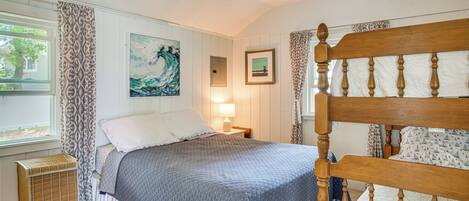 A bedroom with a wooden bed frame, a window with curtains, a bedside lamp, and artwork on the wall.