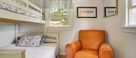 A bedroom with a bunk bed, a single bed, a chair, a window with curtains, and framed pictures on the wall.