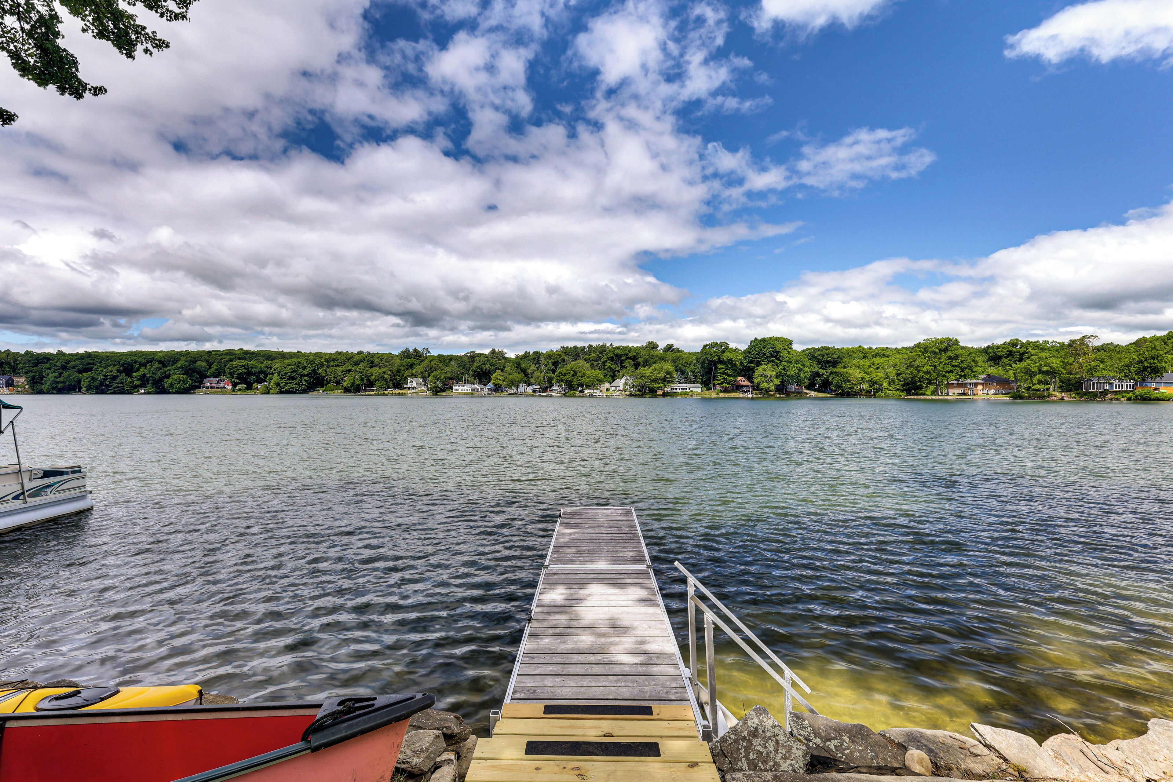 A wooden dock extending into a calm lake, surrounded by trees and houses.