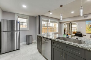 Una cocina moderna con un refrigerador de acero inoxidable, encimeras de granito, un lavamanos doble y un comedor visible a través de un arco.