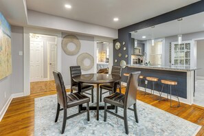 Un comedor con una mesa redonda y sillas, una cocina con barra, y un pasillo que conduce a un dormitorio.