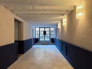 Ein Flur mit Blick auf eine Außenpatio-Terrasse, mit Fliesenboden, einer Tür links und einer Wandleuchte rechts.